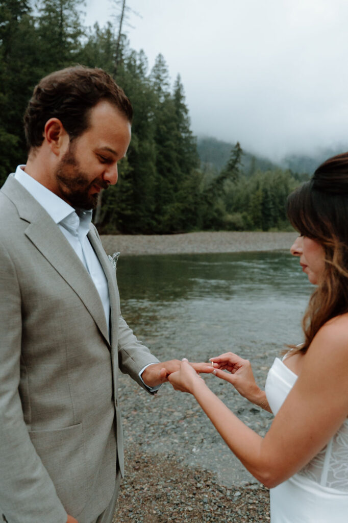 Bride and groom exchange rings on the shore of Avalanche Creek